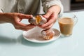 close up of hands breaking apart one of two curd muffins over plate, and glass cup of coffee with milk standing on table. Royalty Free Stock Photo