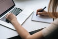 Close-up hands of business woman writing making note in paper notebook sitting at window sill with laptop, working from Royalty Free Stock Photo