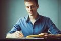 Close up of the hands of a businessman in a blue shirt signing or writing a document on a sheet of notebook.