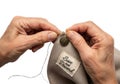 Close up of hands carefully sewing a small button onto a fabric tag with thread Royalty Free Stock Photo