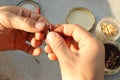 Close-up of the hands of a Caucasian fisherman stringing a red Californian worm on the hook of a fishing rod.