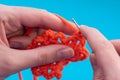 Close up of hands of a caucasian woman crocheting red thread on a blue background, copy space