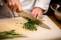 Close-up of hands of chef chopping green onion with knife on cutting board Royalty Free Stock Photo