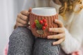 Hands of child holding white mug in winter knitted cover