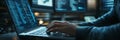 Close-up of hands coding on a laptop in a dimly lit tech office, with multiple monitors displaying lines of code. High