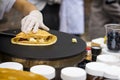 Close-up of hands of cook in gloves preparing rolled up thin Crepe with fresh tasty fruit on frying pan, sweet sauce