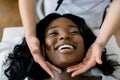 Close-up of hands of cosmetologist woman making special face massage to young pretty African smiling woman lying on Royalty Free Stock Photo