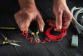 Close-up of hands of electrician foreman while working or cutting red wire. Repair of electrical equipment in workshop of