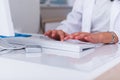 Close up hands of a female physician nurse typing on her white keyboard while sitting on a white desk in a hospital lobby