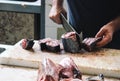 Close up hands of fisherman cutting tuna with a huge cleaver on a wooden board. Blurred tuna meat in the foreground. Local fish