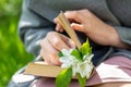 Close-up, hands of a girl in a gray plaid, holding a book on her lap with a bookmark made of twigs with Apple flowers