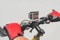 Close-up, the hands of a guy in red gloves on the handlebars of a bicycle with an action camera. On a light background