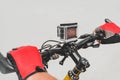 Close-up, the hands of a guy in red gloves on the handlebars of a bicycle with an action camera. On a light background Royalty Free Stock Photo