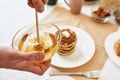 Close up of hands holding a bowl with honey, A stack of sweet tasty pancakes on the table, Process of preparing