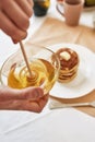 Close up of hands holding a bowl with honey, A stack of sweet tasty pancakes on the table, Process of preparing