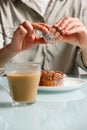 close up of hands holding curd muffin over plate with two another cakes, and glass cup of coffee with milk standing on table Royalty Free Stock Photo