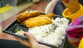 Close up of hands holding plastic spoon and deep fried chicken cutlet torikatsu and rice with black sesame seed on plastic plate Royalty Free Stock Photo