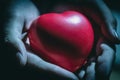 Close up of hands holding heart or love shape in palms on a dark, background