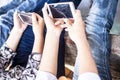 Close up of only hands and legs of teenager sitting on a wall and using smart phones and spending time with friends.