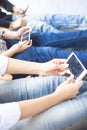 Close up of only hands and legs of teenager sitting on a wall and using smart phones and spending time with friends.