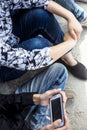 Close up of only hands and legs of teenager sitting on a wall and using smart phones and spending time with friends.