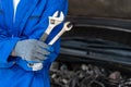 Close up hands of a male car mechanic holding a fix and an adjustable wranches with car engine in background Royalty Free Stock Photo