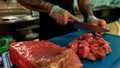 Close up of hands of male cook wearing protective gloves chopping raw pork meat on a plastic board while working in Royalty Free Stock Photo