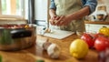 Close up of hands of man in apron peeling garlic while preparing healthy meal, soup in the kitchen. Cooking at home Royalty Free Stock Photo