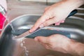 Close-up hands of a man carefully sharpen a knife under a stream of water on a grindstone. Home household sharpening Royalty Free Stock Photo