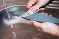 Close-up hands of a man carefully sharpen a knife under a stream of water on a grindstone. Home household sharpening Royalty Free Stock Photo