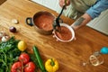 Close up of hands of man pouring tasty soup from pot into bowl. Italian cook preparing traditional meal in the kitchen