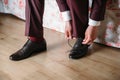 Close-up hands of a man tie laces on black shoes. A businessman in burgundy trousers and socks wears shoes before going Royalty Free Stock Photo