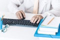 Close-up of hands middle-aged man in white shirt and yellow tie typing on keyboard laptop computer, plastic blue holder with Royalty Free Stock Photo