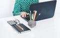 Close-up of hands middle-aged woman in green blouse typing on keyboard laptop, concrete holder with pencils and pens, notebook, Royalty Free Stock Photo