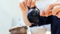 Close-up of hands pouring Chinese green tea from the small ceramic kettle into a small cup with tea strainer in foreground