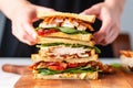 close-up of hands pressing down on finished chicken club sandwich