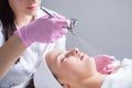 Close-up, hands of a professional cosmetologist doctor, using the apparatus, sprayes a cosmetic product, serum, onto a young Royalty Free Stock Photo