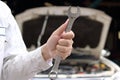 Close up hands of professional young mechanic man holding wrench with car in open hood at the garage background. Auto repair servi Royalty Free Stock Photo