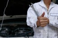 Close up hands of professional young mechanic man showing thumb up as sign of success with car in open hood at the garage backgrou Royalty Free Stock Photo