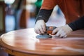 close-up of hands refinishing a hardwood table with a sander