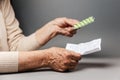 Close up of hands of senior woman holding an instructions of medicines and pills. Gray background. Concept of shopping