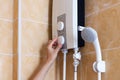 Close-up of hands setting the temperature of water in electric boiler in the shower room.