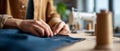 Close-up of hands sewing denim fabric with and thread in a workshop with sewing machine and spools in background Royalty Free Stock Photo