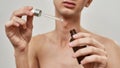 Close up of hands of shirtless young transgender holding pipette and a bottle of hyaluronic acid while posing 