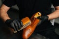 Close-up hands of shoemaker in black gloves polishing light brown leather shoes with brush during restoration working. Royalty Free Stock Photo