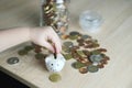 close-up of hands of small child manipulate with metal coins, kid counts, puts euro union money in white piggy bank, concept of