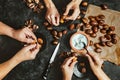 Close up of hands of three people peeling roasted chestnuts on black background. Lifestyle family meal concept. Dark low key photo