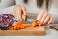 Close up on hands of unknown caucasian woman cutting carrot on the wooden board in the kitchen preparing vegan or vegetarian meal Royalty Free Stock Photo