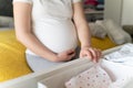 Close up on hands of unknown caucasian woman holding and packing baby clothes at home - Pregnant female preparing jumpsuit for Royalty Free Stock Photo