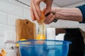 Close up of hands of unrecognizable man breaking egg with knife into blue plastic bowl near steel colander. Cooking. Royalty Free Stock Photo